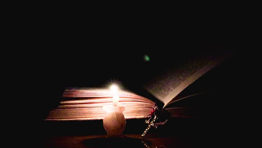 candle flame and cross on an old religious book