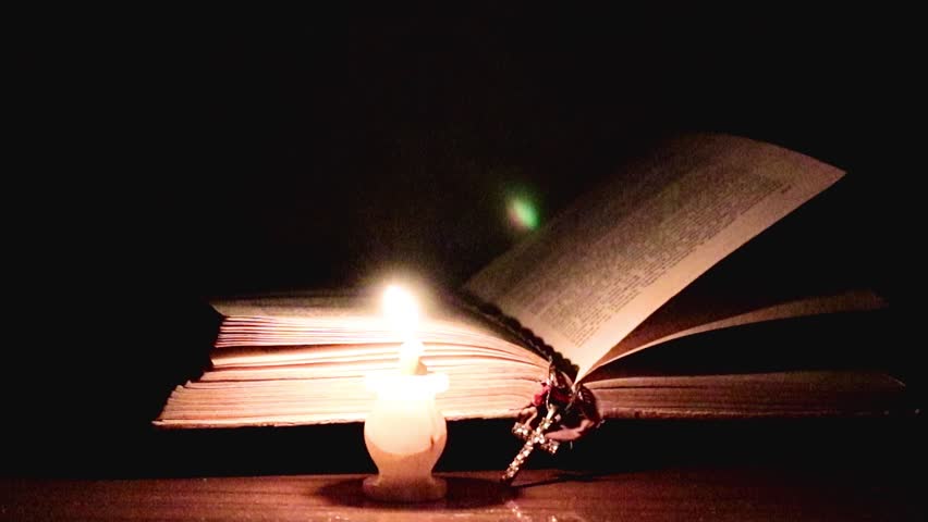 candle flame and cross on an old religious book