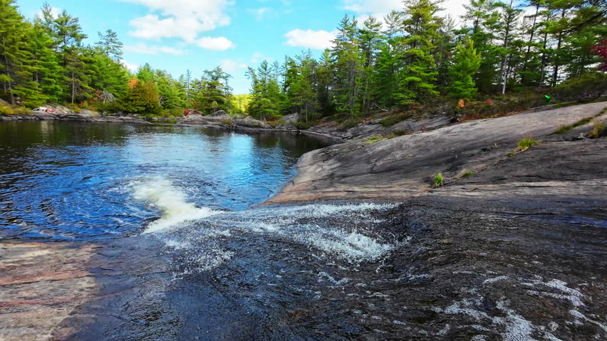 Water flowing over the broad rock ledge of High Falls into a clear pool surrounded by coniferous forest in Algonquin Provincial Park, Ontario, Canada.