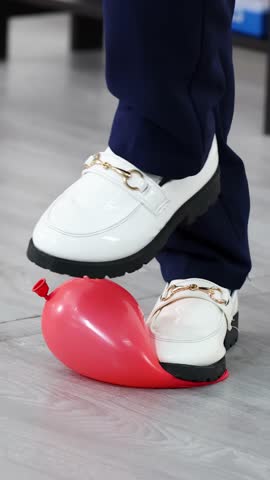 Low angle shot of student stepping on red balloon during classroom STEM physics experiment.
