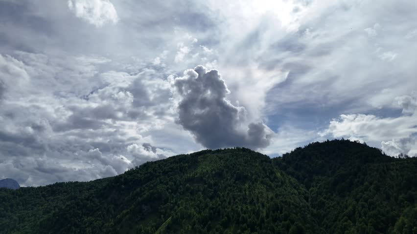 Dramatic backlit storm cloud moving above a densely forested mountain ridge under a moody summer sky