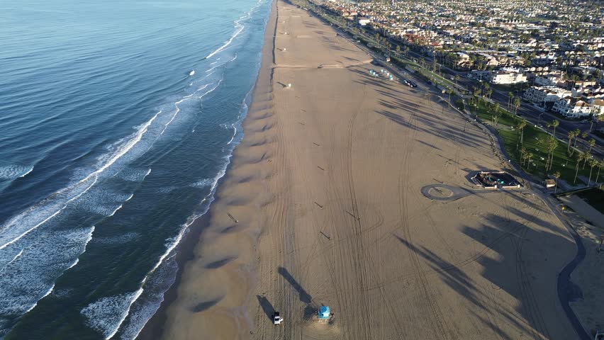 Huntington Beach coastal streets lush green parks meet vast Pacific edge, showing how urban life connects to nature. Rhythmic swells roll onto broad, open shore, highlighting landscape in CA. USA