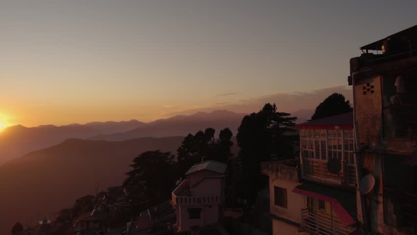 Golden hour sunset illuminates rolling mountains and traditional buildings in a scenic Indian hill station.