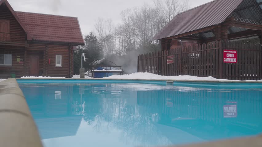 Panoramic view of winter recreation base with wooden cabins, gazebos, outdoor pool and snowy landscape.