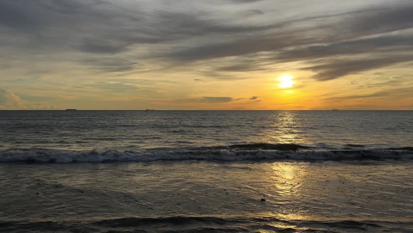 Beautiful seascape featuring the sun setting over the ocean horizon, casting warm golden light across gentle waves beneath a dramatic sky filled with colorful clouds. This tranquil coastal scene captures the beauty of nature, travel, relaxation, and the peaceful atmosphere of twilight by the sea.