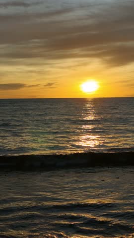 Beautiful seascape featuring the sun setting over the ocean horizon, casting warm golden light across gentle waves beneath a dramatic sky filled with colorful clouds. This tranquil coastal scene captures the beauty of nature, travel, relaxation, and the peaceful atmosphere of twilight by the sea.
