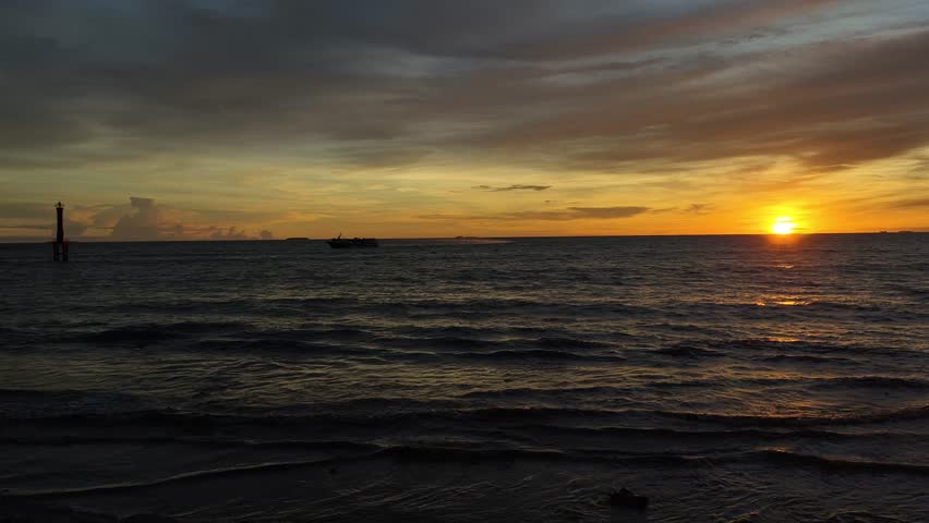 Beautiful seascape featuring the sun setting over the ocean horizon, casting warm golden light across gentle waves beneath a dramatic sky filled with colorful clouds. This tranquil coastal scene captures the beauty of nature, travel, relaxation, and the peaceful atmosphere of twilight by the sea.