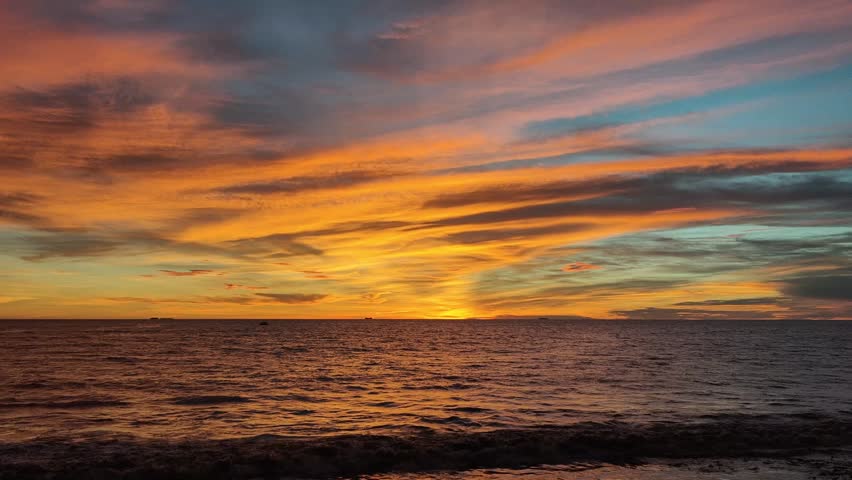 Beautiful seascape featuring the sun setting over the ocean horizon, casting warm golden light across gentle waves beneath a dramatic sky filled with colorful clouds. This tranquil coastal scene captures the beauty of nature, travel, relaxation, and the peaceful atmosphere of twilight by the sea.