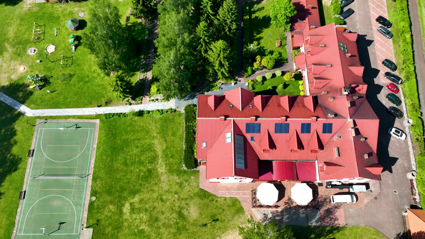 Birds eye view of a lakeside hotel in Masuria, Poland, featuring ecofriendly solar panels, a sports court, and playground. Perfect for sustainable travel and real estate content.