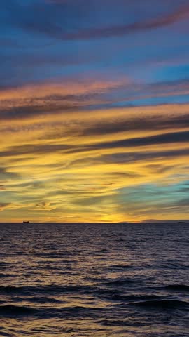 Beautiful seascape featuring the sun setting over the ocean horizon, casting warm golden light across gentle waves beneath a dramatic sky filled with colorful clouds. This tranquil coastal scene captures the beauty of nature, travel, relaxation, and the peaceful atmosphere of twilight by the sea.