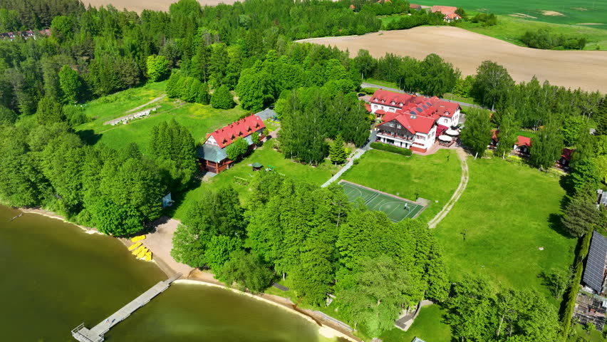 Cinematic aerial shot of a beautiful hotel complex and guest houses situated on the lush green shores of Lake Goldapiwo in the Masurian Lake District of Poland.