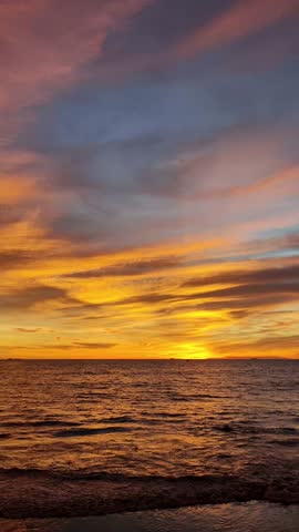 Beautiful seascape featuring the sun setting over the ocean horizon, casting warm golden light across gentle waves beneath a dramatic sky filled with colorful clouds. This tranquil coastal scene captures the beauty of nature, travel, relaxation, and the peaceful atmosphere of twilight by the sea.