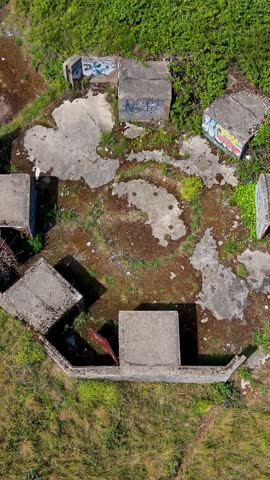Chadwell Heath ZE1 gun emplacements seen from above as vertical drone reverses and rises, revealing octagonal concrete AA battery remains, overgrown grassland, WWII heritage landmark in London, UK.
