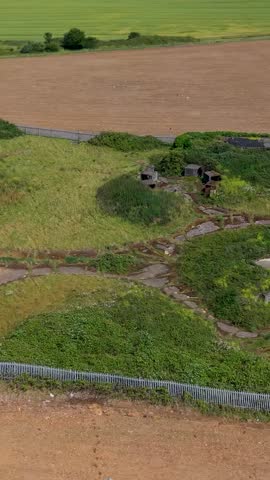 ZE1 gun emplacements, Chadwell Heath verticaerial orbit showing WWII anti-aircraft battery concrete bunkers, magazine huts and access paths amid overgrown grassland on former RAF London defences site.