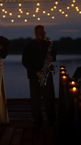 Silhouetted saxophonist playing on a lakeside deck at dusk