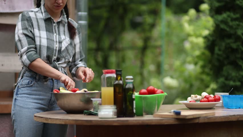 Young woman in a plaid shirt slicing fresh zucchini and adding it to a salad bowl. Healthy lifestyle and organic food preparation in a garden