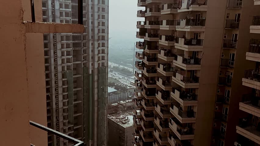 High-rise residential apartment buildings with an under-construction tower viewed from an elevated balcony in an urban cityscape.