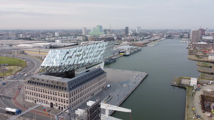 Rotating drone footage around Antwerp’s Port House, showcasing the surrounding dock basin and the city skyline in the background under bright overcast skies.