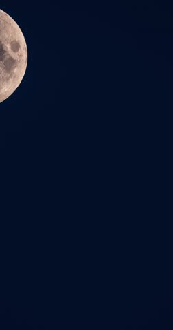Vertical time lapse video of a sharp close-up half moon in its first quarter phase in a deep blue twilight sky.