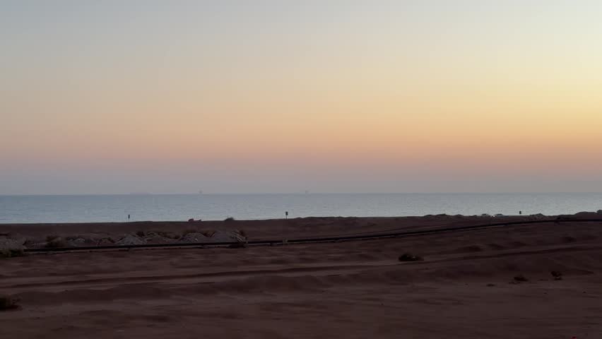 Wide scenic shot of the expansive sandy desert coastline and the calm Red Sea horizon during the twilight hour in Egypt. Atmospheric and minimal landscape.