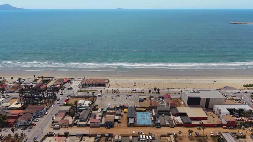 Aerial drone view of a beachfront town in Baja California with a wide sandy beach and calm turquoise water.