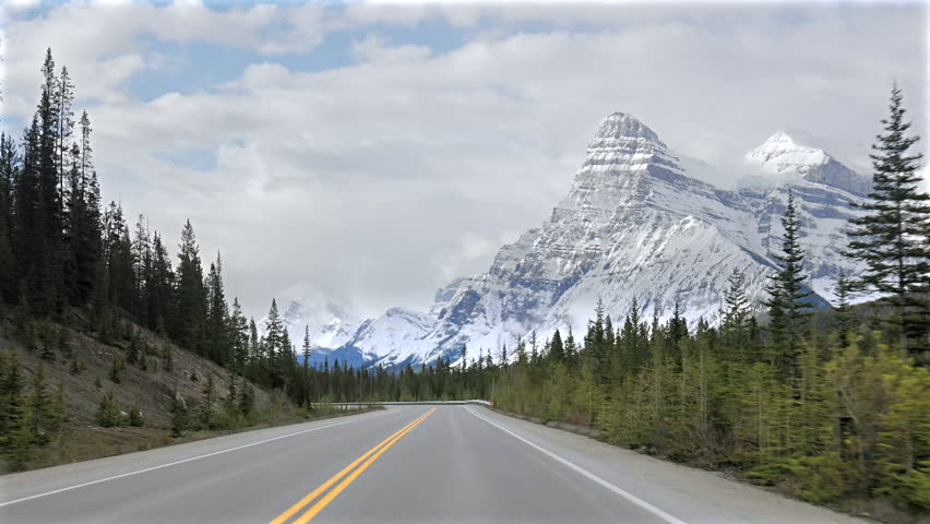 Car driver point of view video travelling on the Icefields Parkway through Banff National Park, with snow peaked mountains, pine forest and winter road trip scenery in Alberta Canada.