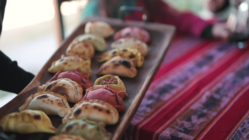 Close-up of Assorted Colorful Argentine Empanadas Served on Long Rustic Wooden Platter in Restaurant