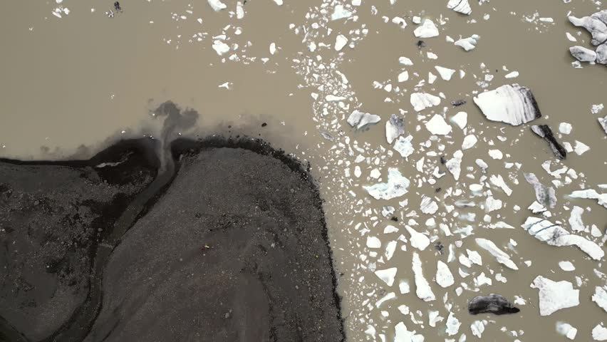 flying over a brown lake with scattered pieces of icebergs