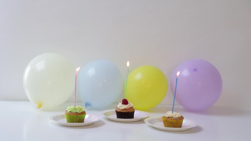 Three tasty cupcakes with lit birthday candles arranged with colorful balloons for a festive party celebration.