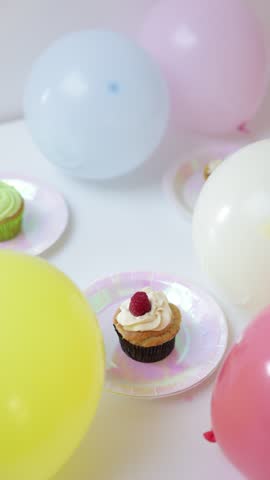 Tasty cupcakes with frosting on small shiny plates decorated with festive balloons for a birthday celebration.