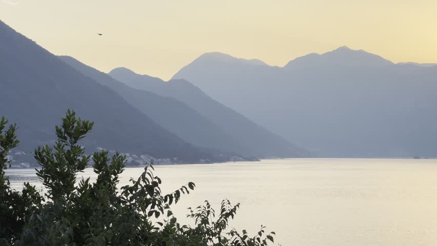 Golden sunset over Kotor Bay with calm sea water and hazy mountains, Montenegro. Scenic evening landscape of Adriatic sea bay with sound