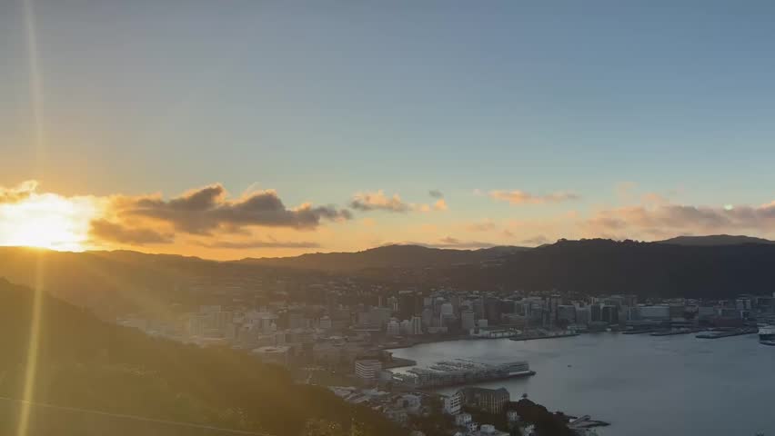 Panoramic sunset view from Mount Victoria Lookout overlooking Wellington, New Zealand. Breathtaking city, harbor and surrounding hills illuminated by warm evening light in a peaceful cinematic landscape.