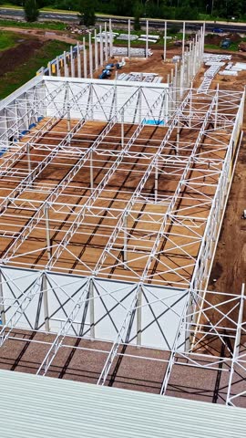 Aerial view of white steel skeleton rising over sandy ground as large industrial facility takes shape amid green landscape