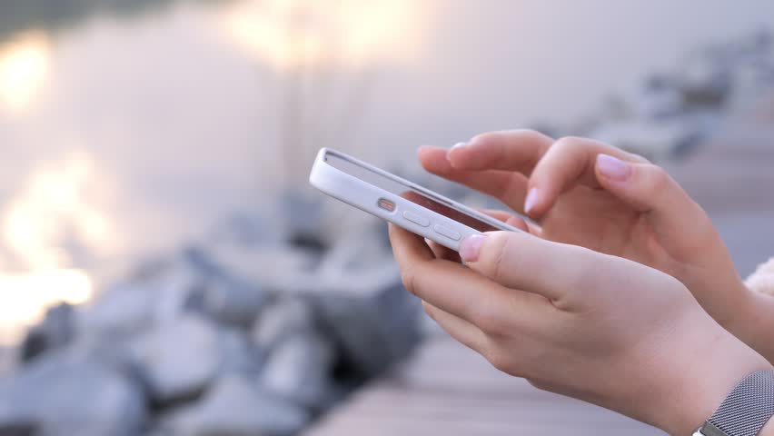 Close-up of hands holding and swiping on a smartphone. Fingers move confidently across the screen. Soft natural lighting enhances the scene. Person appears focused and relaxed while using their device