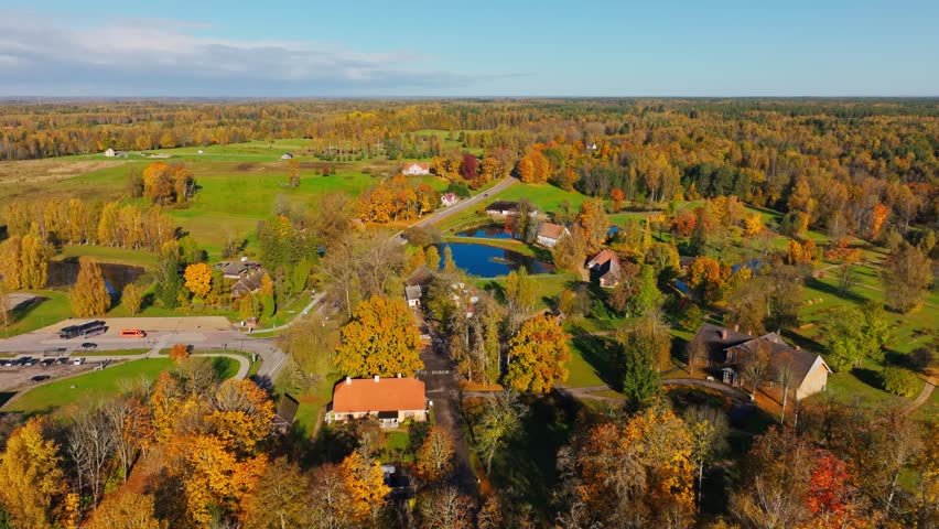Cinematic flight, autumn countryside surrounds lakes, forests, homes, Sigulda