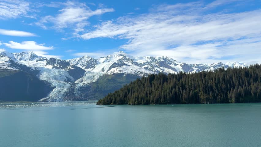 Mountains of Alaska covered in ice and snow, with water reflecting them. Ice floats on the surface, and a clear sky stretches above. This location highlights nature