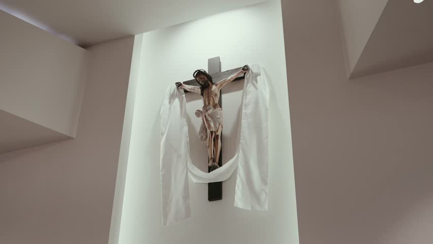 Wooden crucifix with painted Jesus Christ figure and white fabric drapes mounted on church wall