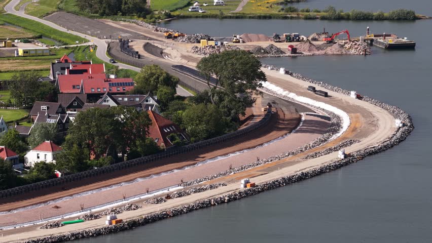 Extensive construction work on a dike showing heavy machinery reinforcing the coastal flood defenses to protect a small village from rising sea levels and extreme weather