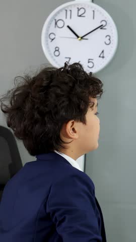 A young boy in a suit points at data charts on a whiteboard during presentation.