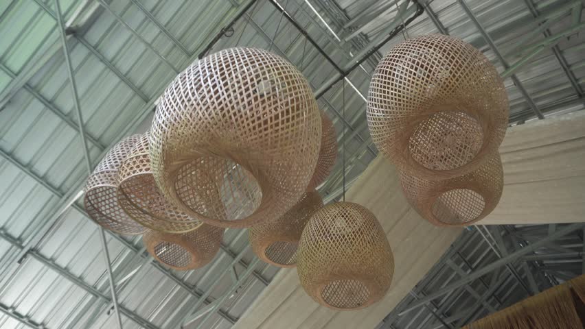 Elegant cluster of woven bamboo pendant lamps swaying softly in wind, viewed from below against bright metal ceiling structure.