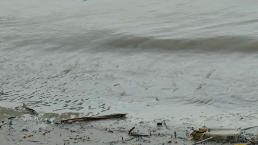 Muddy river water with foam bubbles washing onto sandy shore 