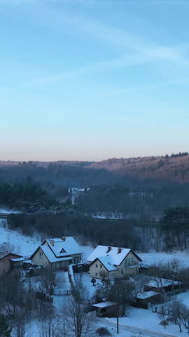 Cinematic vertical shot of residential houses and forest covered in fresh snow during a cold winter morning in , Poland.