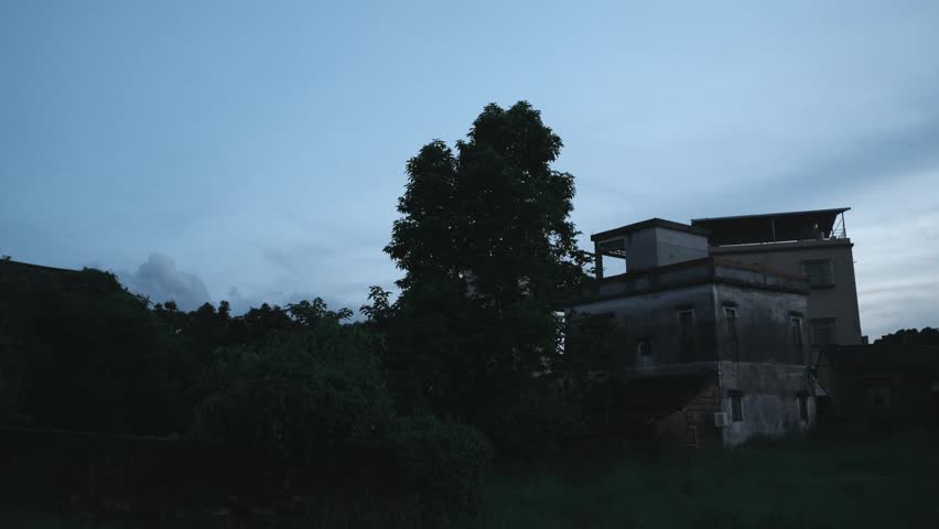 Old abandoned building with overgrown trees at dusk in rural India faded concrete structure,