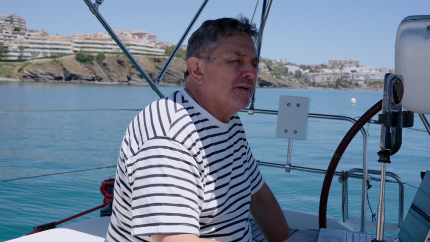 Mature man with a striped t-shirt recording a vlog on his boat while sailing on the sea