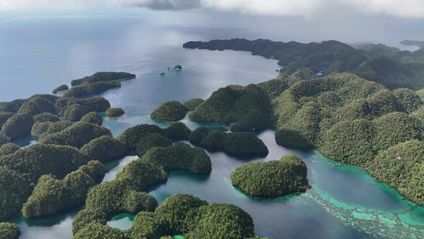 Breathtaking wide-angle aerial drone view of numerous small, dome-shaped jungle islands scattered across a calm, clear turquoise ocean lagoon with visible coral reefs in Siargao, the Philippines.