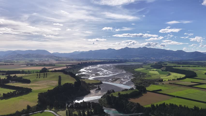 Aerial view of braided river channels winding through fertile farmland on the South Island of New Zealand, highlighting agricultural landscapes, waterways, and mountain horizons.