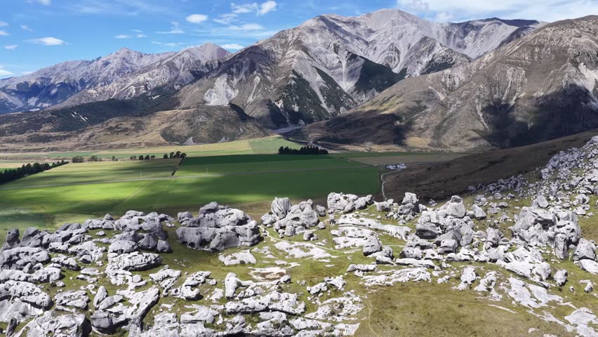 Limestone boulders scatter across open grassland beneath mountains on New Zealand South Island