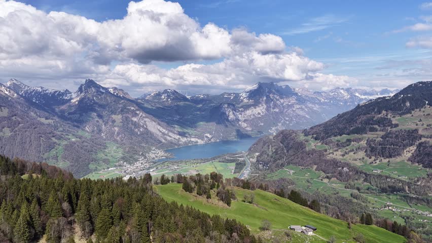 Drone footage overlooking a dramatic alpine lake surrounded by the majestic Swiss Alps under towering clouds.