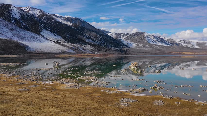 Dynamic drone footage capturing the natural beauty of mono lake in california. snow-capped mountains reflect in the calm, turquoise water, showcasing unique tufa formations and a vibrant, tranquil landscape.