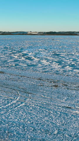 Vertical view of a frozen coastline during winter in Rewa, featuring jagged ice floes, snowcovered ground, and a clear blue sky. Cinematic winter landscape for travel and climate content.